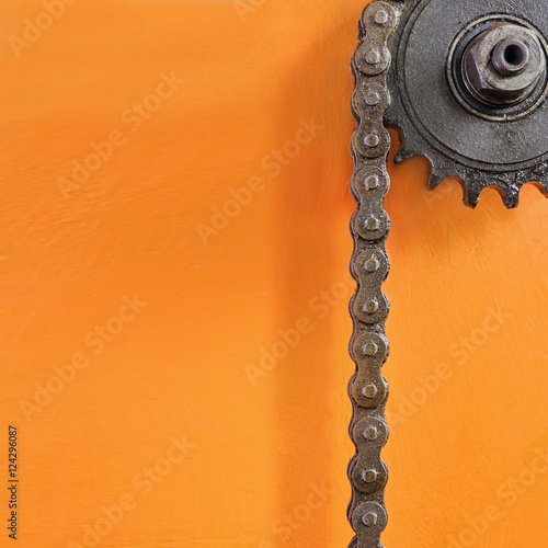 Metal cogwheel and black chain on orange background with empty space.