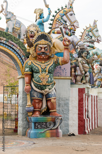 Madurai, India - October 21, 2013: Colorful statues with Karuppana Sami folk deity up front at his shrine near Nagamalai Village outside Madurai. Horses, lion, snake and red-skinned, armored giant.