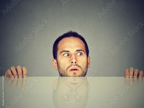worried man looks at something peeking from under the table