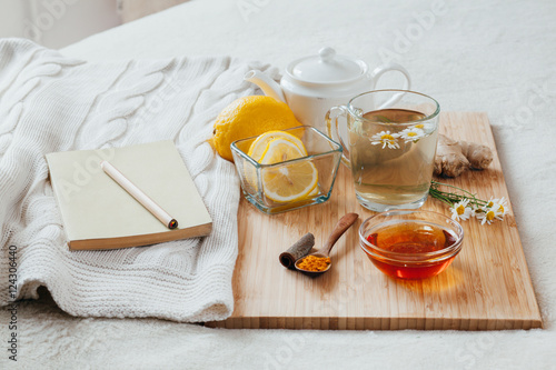 Herbal tea with chamomile flowers, turmeric and honey on a wooden board. Treatment of hot drink with ginger. Treatment of folk remedies in bed. Leisure with a book.