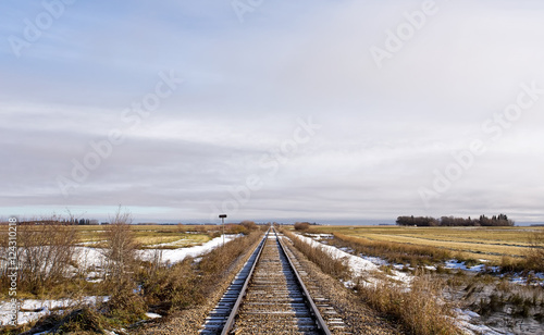 Railway track dividing harvested fields running straight into the far distance in a barren rural landscape in late autumn