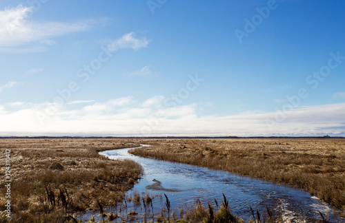 A stream of water winding through a harvested field in a late autumn rural landscape