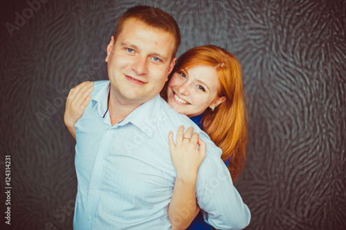 Smiling woman with red hair hugs her happy man from behind