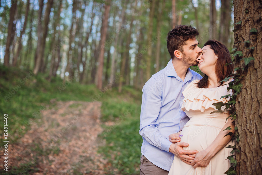 handsome husband and his pregnant wife standing in the forest