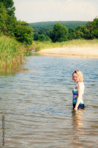 A woman stands in the river in a bathing suit