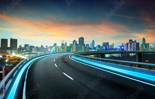 Blue neon light highway overpass motion blur with city skyline background , night scene .