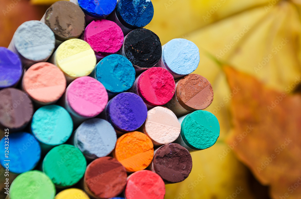 different colored pastel chalks on background of autumn leaves Stock