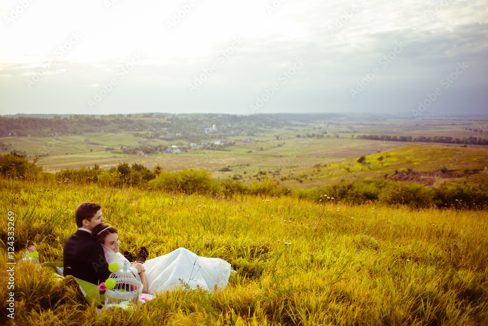 Newlyweds lie on the hill admiring fields under the grey sky