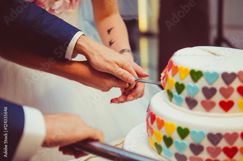 Bride and groom cut white wedding cake decorated with colorful h