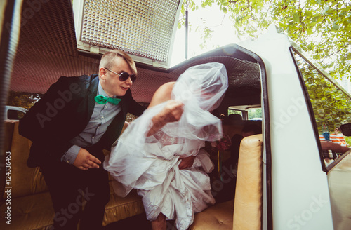 Groomsman helps man dressed like a bride step out the limousine