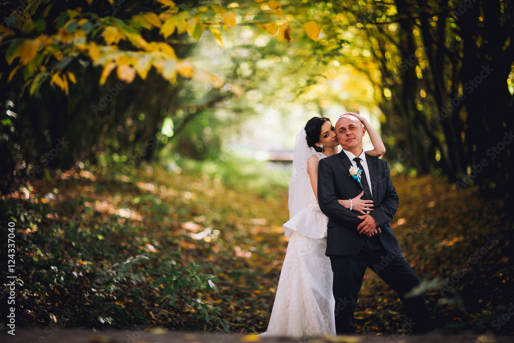 Kissing bride and groom in their wedding day near autumn tree in the forest Kissing bride and groom in their wedding day near autumn tree in the forest