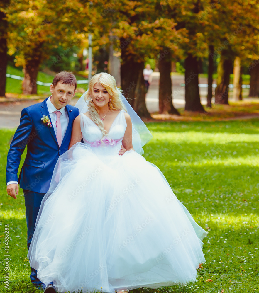 Groom in blue suit walks with a luxurious bride on the lawn Groom in blue suit walks with a luxurious bride on the lawn