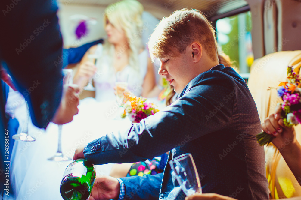 Obraz premium Groomsman pours champagne in the glass while sitting in limousin