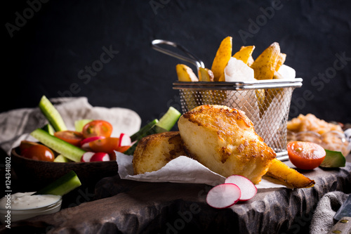 Fish and chips. Fried fish fillet with homemade baked potatoes and fresh salad on wooden cutting board. photo