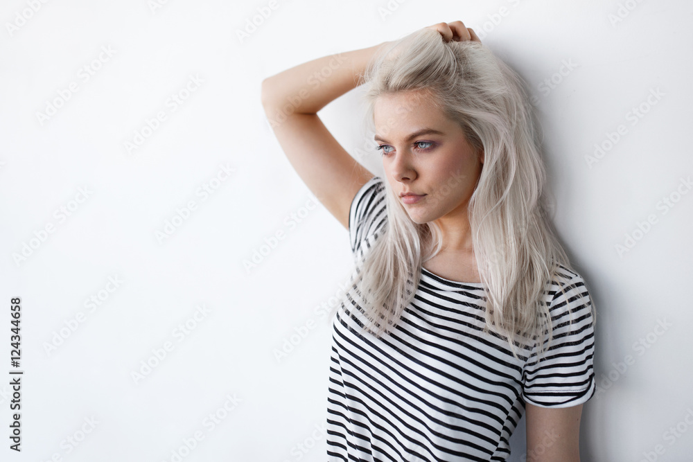 Obraz premium beautiful young blond woman posing while leaning on white wall