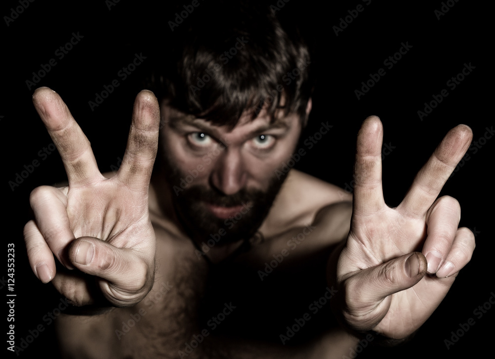 Dark portrait of scary evil sinister bearded man with smirk, shows sign of Victory. strange Russian man with a naked torso Dark portrait of scary evil sinister bearded man with smirk, shows sign of Victory. strange Russian man with a naked torso