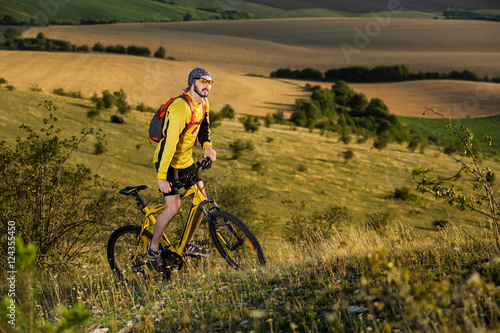 Fototapeta Naklejka Na Ścianę i Meble -  Young cyclist on a rural road through green spring meadow