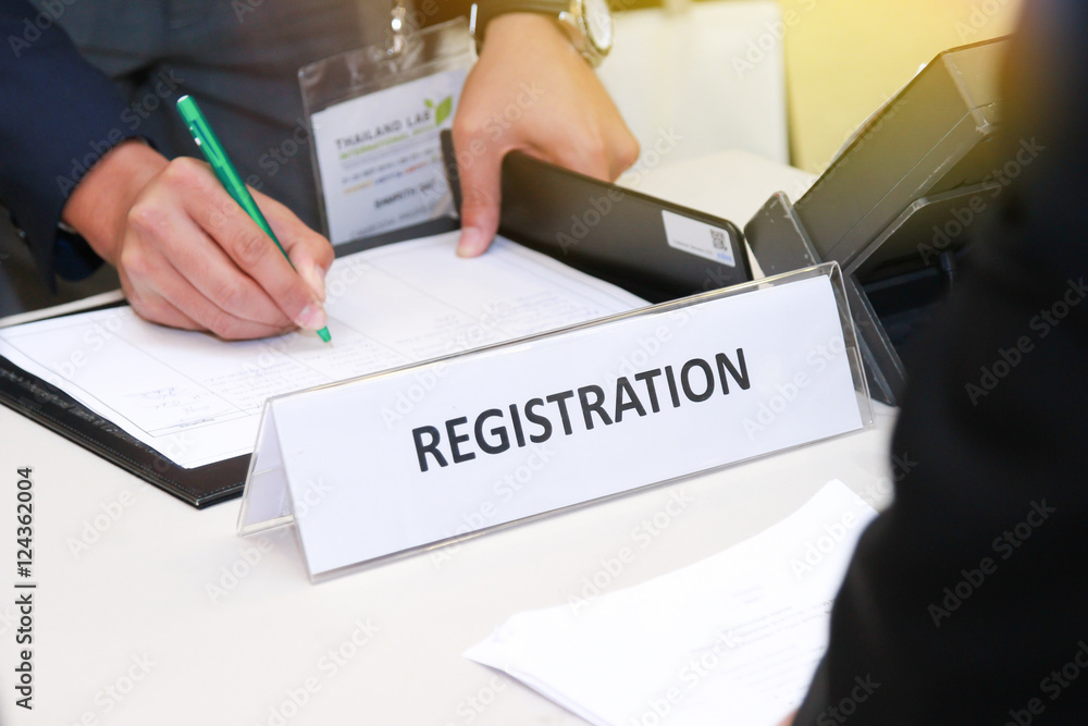 close-up of registration desk in front of conference center with Businessman Writing on the Table close-up of registration desk in front of conference center with Businessman Writing on the Table