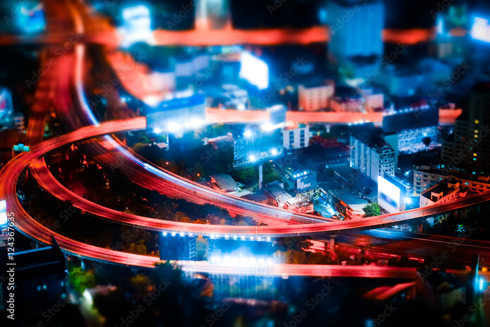 Obraz premium Tilt shift blur effect. Futuristic night cityscape aerial view panorama with illuminated skyscrapers and city traffic across streets. Bangkok, Thailand
