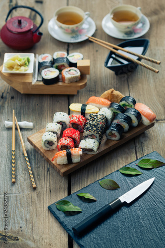 A variety of sushi and green tea set on rustic wooden table.