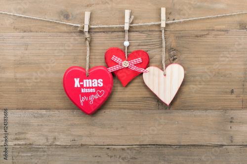 Christmas message concept: Three different wooden hearts hanging on clothesline. Wooden wall as background.