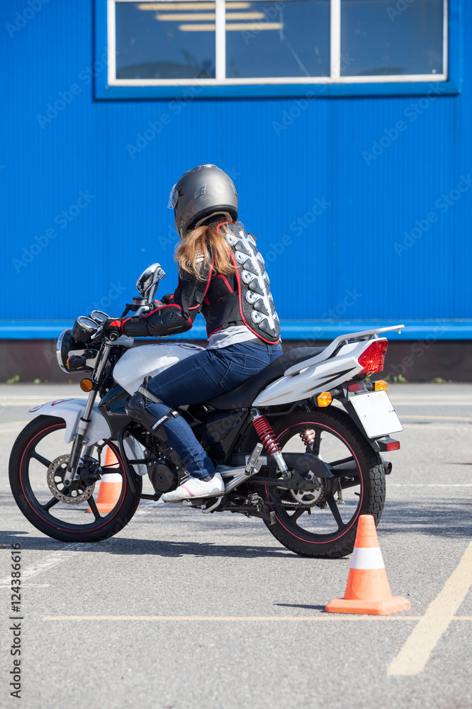 Naklejka premium Początkujący kobieta robi ćwiczenia wokół pachołków na motocyklu w motordrome treningu umiejętności. Rosyjska szkoła kierowców