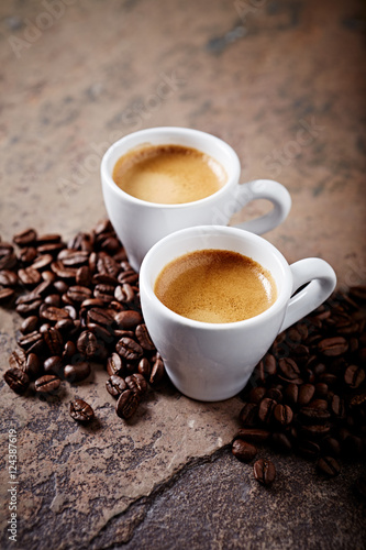 Two cups of coffee with coffee beans on a stone background