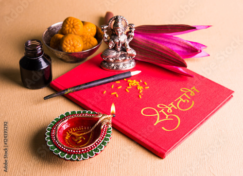 An auspicious Indian writing Shubha Labh means 'Goodness' & 'Wealth', over Red accounting note book / 'bahi khata' with goddess Laxmi, diya, sweets and lotus and pen with ink on laxmi pujan, on diwali