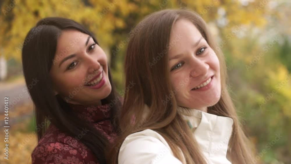 Two pretty girls walking in autumn park, make selfie, fooling around on camera