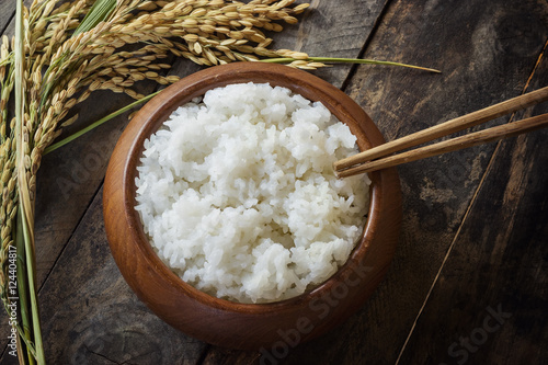 cooked rice in a cup with the ear of paddy rice form the field of farmland put on right side, It has been on the wooden table background.