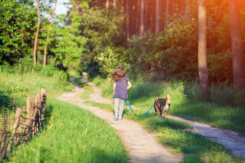 Little girl walking with a dog on the road in the forest