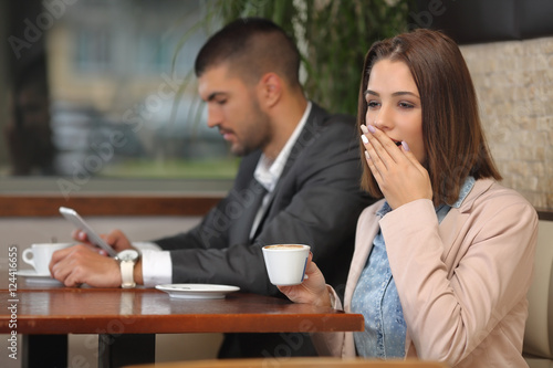 Portrait of young business team on a break in a coffee shop. Beautiful young businesswoman is yawning while drinking her coffee while businessman is using phone in the background.