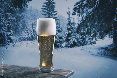 Glass of beer on wooden table against winter nature background.