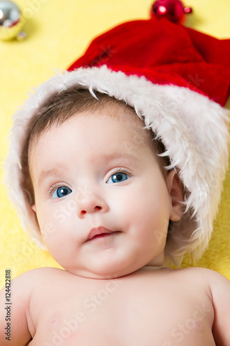 Portrait of baby in a red Santa hat with balls on the New year tree. Beautiful little celebrates Christmas. holidays.