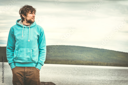 Young Man standing alone outdoor with scandinavian mountains and lake on background Lifestyle and melancholy emotions concept © EVERST