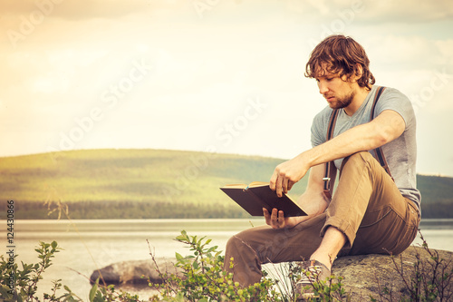 Young Man reading book outdoor lake on background Education Lifestyle Travel concept Summer vacations © EVERST