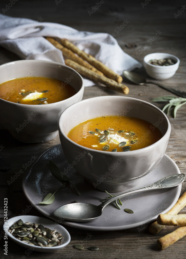 Pumpkin cream soup in grey bowls on rustic wooden table Pumpkin cream soup in grey bowls on rustic wooden table