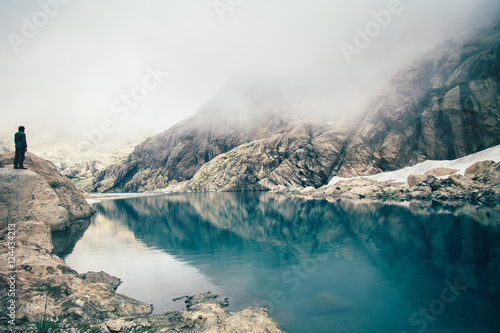Man Traveler standing alone on cliff lake and foggy mountains on background Travel Lifestyle inspiring concept outdoor