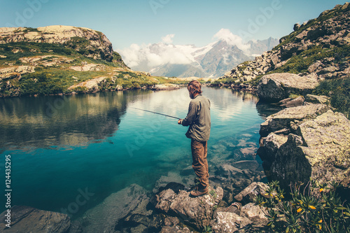 Young Man fishing on Lake with rod mountains landscape on background Travel Lifestyle concept summer vacations