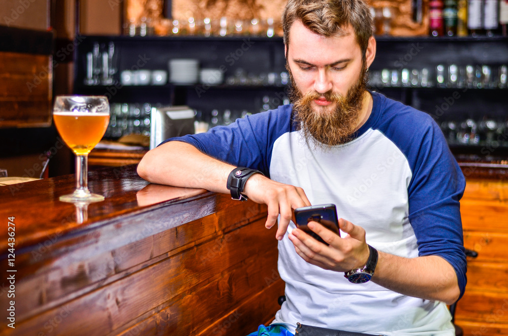 a guy sitting at the bar with a smartphone in your hands and a glass of beer