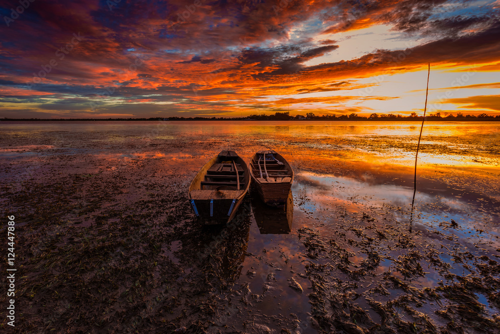 Fototapeta premium Small fishing boats beached on the riverbank in the park at sunset. Shows a silhouette of a beautiful sky reflected from the water surface.
