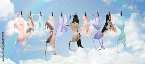 Beautiful collection of various colorful lingerie sets and lace underwear drying on a clothesline with clothespins under a blue sky with clouds, feminine fashion background