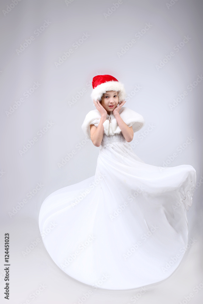 Full-length portrait of little girl in long white dress and Santa helper hat over light background Full-length portrait of little girl in long white dress and Santa helper hat over light background