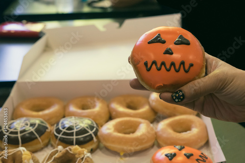 woman hand hold halloween pumpkin orange donut and donut set in paper box ready to eat /  woman hand hold halloween donut