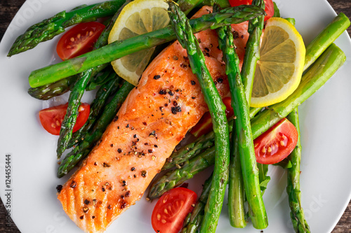 Fried salmon with asparagus, tomatoes, lemon, yellow lime on white plate