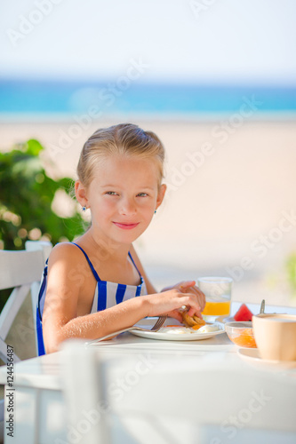 Adorable little girl having breakfast at cafe with sea view © travnikovstudio