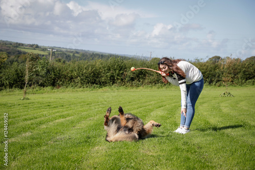 Teenage girl plays with her dog outside in a field, the dog rolls over on command © Nicky Rhodes
