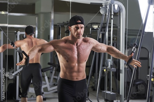 Handsome powerful athletic man doing cable crossover exercise. Strong bodybuilder with perfect abs, chest and arms.