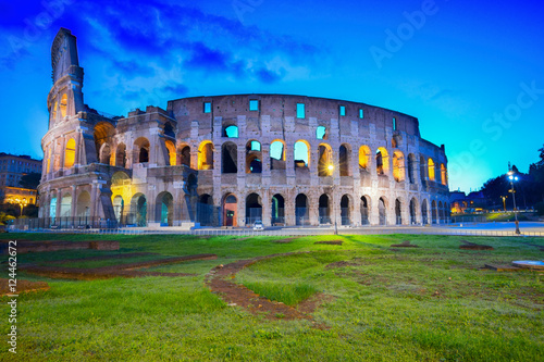 view of Colosseum with green lawn illuminated at night in Rome, Italy