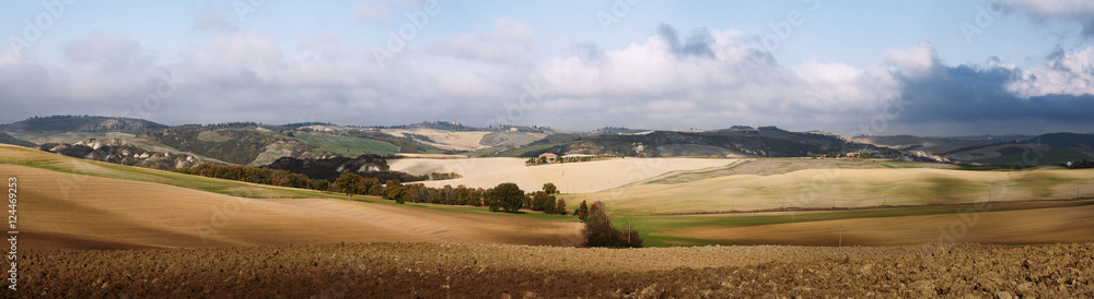 Wavy fields in Tuscany with shadows and farms, Italy. Natural outdoor seasonal summer background with blue sky and clouds.